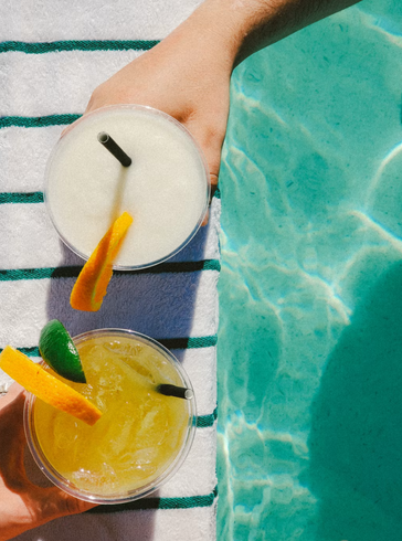 Two cocktails held beside a swimming pool